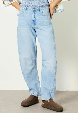 Jean taille haute bleu clair à coupe décontractée, porté avec des mocassins marron à enfiler et un haut à manches à motifs.