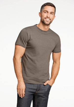 Männer T-Shirt mit kurzen Ärmeln aus olivgrünem Baumwoll-Jersey, mit Rundhalsausschnitt, kombiniert mit dunklen Jeans. Glatte Textur, taillierte Passform.