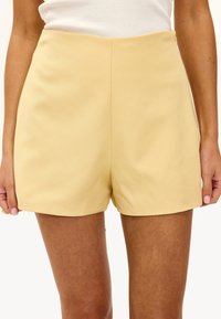Shorts jaunes ajustés avec une texture lisse, taille haute et lignes épurées, sans poches visibles ni embellissements.