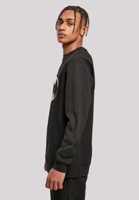 Felpa nera in tessuto di cotone, con scollo rotondo e maniche lunghe. Presenta un logo grafico prominente sulla parte anteriore.