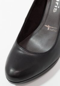 Chaussure fermée pour femmes en cuir noir avec semelle intérieure rembourrée, portant la marque "touch it", sur fond blanc.