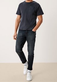 Camiseta de manga corta azul marino con un bolsillo, combinada con jeans oscuros y zapatillas blancas. Casual, de corte relajado y con una tela texturizada.