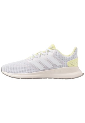 Lichtgrijze sportsneaker met witte veters, witte Adidas-strepen, gele accenten en een gedempte zool.