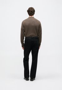 Suéter de punto marrón y jeans de mezclilla negros, vistos desde atrás. El suéter tiene una textura suave, los jeans están ligeramente desgastados con un corte clásico.