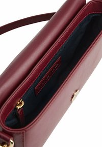 Bordeauxfarbene Lederhandtasche mit glatter Textur, Reißverschlussfach, goldenen Beschlägen und navy Innenfutter. Mit einem Schultergurt ausgestattet.