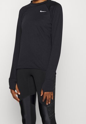Personne portant un haut Nike noir à manches longues avec des trous pour les pouces et des leggings noirs avec des panneaux texturés et des détails latéraux à pois.