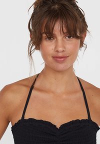 Top halter smockato nero con bordi arricciati e spalline sottili. Texture liscia con silhouette aderente. Design semplice e versatile.