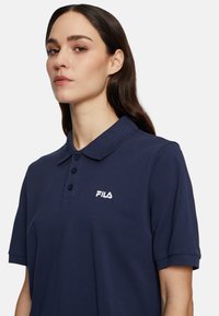 Navyblauwe polo gemaakt van textuurstof, met een drieknops sluiting en een geborduurd wit FILA-logo op de linkerborst.