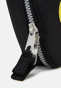 Borsa in tessuto nero con una zip argentata prominente, dotata di un doppio cursore e una tracolla nera testurizzata per un facile trasporto.