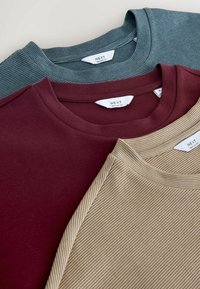 Kolme crew-neck T-paitaa: tummanvihreä raidallinen, yksivärinen burgundinpunainen ja beige raidallinen. Kaikissa on pehmeä tekstuuri ja etiketti, jossa lukee "NEXT."