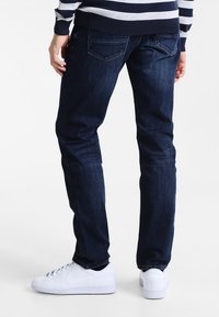 Mörkblå denimjeans med slim fit, med synlig stygning och bakfickor. Kombineras med vita sneakers.