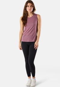 Ärmelloses Sporttop in Helllila, aus feuchtigkeitsableitendem Material. Kombiniert mit schwarzen Leggings und weißen Turnschuhen für einen sportlichen Look.