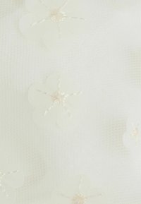 Tessuto in tulle bianco con applicazioni floreali e cuciture di colore crema. La texture è trasparente con una qualità delicata e leggera.