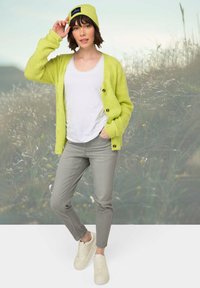 Cárdigan verde lima con botones, top blanco, pantalones grises y zapatillas crema. La modelo lleva un gorro a juego con un parche de logo.