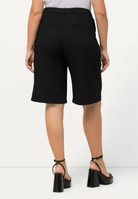Zwarte bermuda shorts met een elastische tailleband, voorzien van twee achterzakken en een gladde textuur. Gecombineerd met chunky zwarte sandalen met een hoge hak.