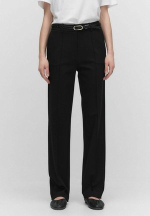 Zwarte hoge taille broek met een getailleerde pasvorm, voorzien van plooien aan de voorkant en een gevlochten riem. Gecombineerd met een wit t-shirt en zwarte ballerina's.