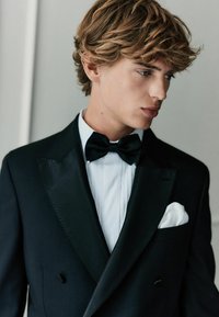 Schwarzes Smokingjackett mit satinierten Revers, weißes, plissiertes Hemd, schwarze Fliege und ein weißes Einstecktuch. Strukturierten Stoff, taillierte Passform.