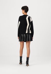 Black sweater with white zigzag pattern on sleeves, paired with a pleated black leather skirt and knee-high black boots.