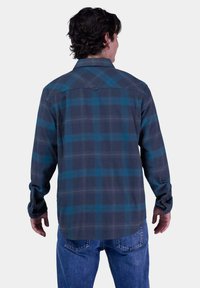 Camisa de cuadros en gris oscuro y azul verdoso, con un cuello abotonado y mangas largas. La tela parece suave y tiene un ajuste relajado.