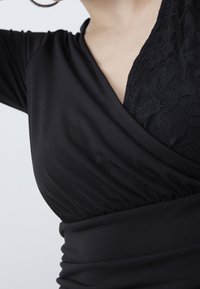 Černý top s překládaným designem, shromážděnou texturou a krajkovým panelem na jedné straně. Hladká tkanina s přiléhavým siluetou a krátkými rukávy.