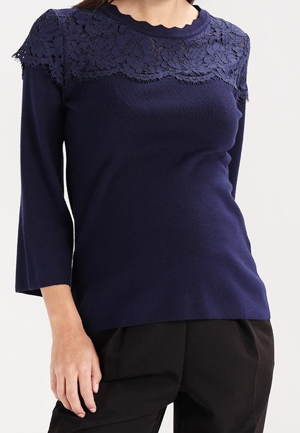 Top de manga larga azul marino con detalles de encaje en la parte superior del pecho y los hombros, combinado con pantalones negros.