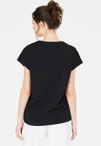 Black short-sleeve top in soft material with a relaxed fit. Round neckline, subtle stitching details, and a curved hem at the back.