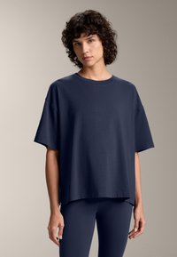 Tricou supradimensionat de culoare bleumarin, fabricat din bumbac moale, cu mâneci scurte, guler rotund și tiv drept cu fante laterale.