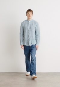 Hellblaues Leinen-Hemd mit Knöpfen, lange Ärmel, lockerer Schnitt, kombiniert mit dunkelblauen Jeans und weißen Sneakers. Einfaches Design, keine Muster.