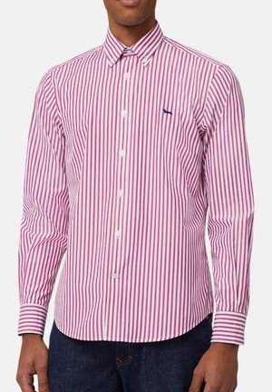 Homme portant une chemise à manches longues boutonnée avec des rayures verticales rouges et blanches et un petit logo sombre sur la poitrine gauche.