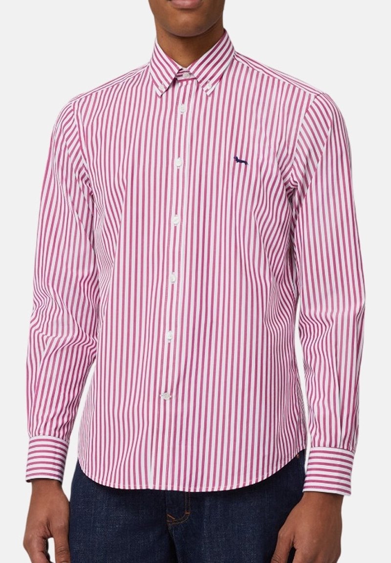 Mężczyzna ubrany w koszulę na guziki z długim rękawem, z pionowymi czerwono-białymi paskami i małym ciemnym logo na lewej piersi.