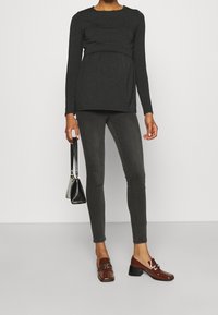 Graviditets långärmad topp i mörkgrått, med empiremidja; kombinerad med mörkgrå skinny jeans och glansiga bruna låga klackskor.