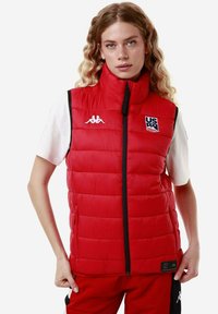 Gilet imbottito rosso con colletto alto, chiusura a zip e tasche laterali. Presenta accenti del logo bianco e una texture trapuntata in tutta la sua superficie.