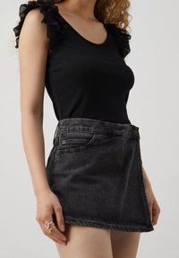 Černý žebrovaný top s krajkovými rukávy s volánky, v kombinaci s černou džínovou sukní s vysokým pasem. Sukně má boční kapsy a nepouštěný lem.