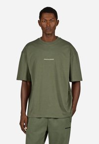 Ελαιόχρωμο oversized t-shirt φτιαγμένο από μαλακό βαμβάκι, με στρογγυλή λαιμόκοψη και κοντά μανίκια. Στο μπροστινό μέρος υπάρχει ένα μικρό λογότυπο "PEGADOR".