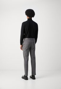 Črna majica z dolgimi rokavi v kombinaciji s svetlo sivimi hlačami. Hlače imajo zadnje žepe z nežnim šivom. Model nosi črne čevlje.