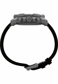 Orologio grigio con quadrante testurizzato, due pulsanti e un cinturino in tessuto nero con una fibbia argentata. Logo Timex visibile sul lato.