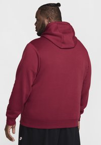 Sudadera color burdeos con capucha y cordón, puños y dobladillo acanalados. Textura suave con un corte holgado, presenta un diseño liso y sin logotipos visibles.