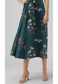 Robe midi florale en vert foncé avec des motifs de fleurs roses et blanches. Présente une silhouette fluide et un détail en tissu noué à la taille.