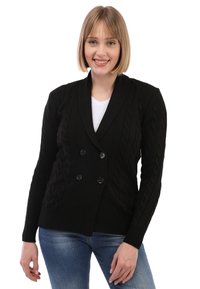 Schwarzer Strickcardigan mit Doppelknopf-Design, großen Knöpfen und langen Ärmeln. Trägt man über einem weißen T-Shirt und blauen Jeans.