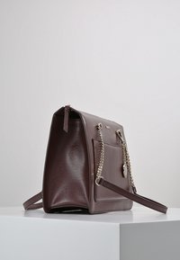 Tmavě burgundská kožená kabelka se strukturovaným tvarem, stříbrnými řetízkovými detaily a přední kapsou. Má odnímatelný ramenní popruh.