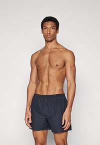 Marineblaue Schwimmshorts aus leichtem Stoff. Sie verfügen über einen elastischen Bund und einen Knopf vorne, mit einer lockeren Passform und glatter Textur.