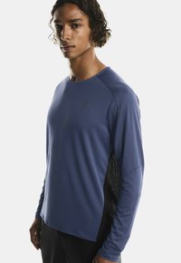 Sügavsinine pikki varrukatega sportlik särk, millel on tekstuuriga aktsendid ja mustad külgpanelid. Valmistatud kergest, niiskust imavast materjalist.