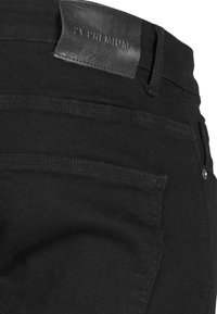 Jean en denim noir avec une finition texturée, présentant une étiquette en cuir portant le nom "RY PREMIUM" au niveau de la taille et des poches arrière standard.