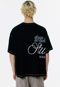 Czarny bawełniany t-shirt z białymi grafikami tekstowymi na plecach, okrągłym dekoltem i krótkimi rękawami. Kontrastowe szwy na szwach.