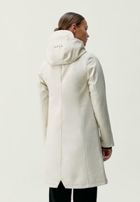 Biely kabát po kolená so štruktúrovanou kapucňou, detailmi na zadnom šve a hladkou textúrou; obsahuje logo blízko otvoru kapucne.