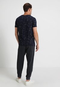 Marinblå bomullströja med ett subtilt abstrakt mönster, i kombination med mörkgrå tapered byxor och vita sneakers. Standard passform, korta ärmar.