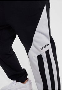 Schwarze Jogginghosen mit einem weißen Einsatz, schwarzen Streifen und einem Logo am Unterschenkel. Hergestellt aus einem weichen, atmungsaktiven Material.
