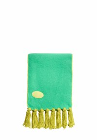 Lysegrønt tæppe lavet af blødt stof, der har gule kvaster langs kanten og en lille gul oval etiket på den ene side.