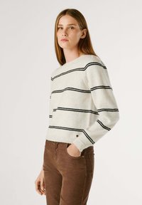 Crème trui met zwarte horizontale strepen, ronde halslijn en lange mouwen, gecombineerd met een paarse broek. Zachte textuur, casual pasvorm.
