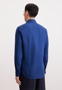 Marineblauw overhemd met lange mouwen, klassieke kraag en met knopen bevestigde manchetten. Glad materiaal, getailleerde pasvorm en geen opvallende patronen of accenten zichtbaar.